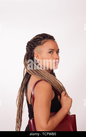 Portrait d'une fille européenne avec des tresses africaines, rasé des temples et un sac rouge foncé sur un fond blanc Banque D'Images