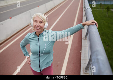 Professionnels des femmes plus âgées avec des écouteurs debout devant des caméra sur racetrack à stade tout en écoutant de la musique Banque D'Images