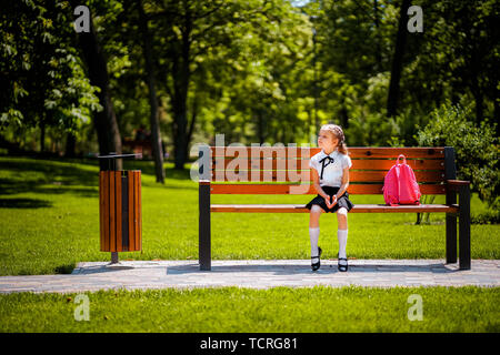 Retour à l'école. Happy cute industrieux enfant assis sur le banc et à pensivement sur le côté. Concept de l'éducation réussie. Banque D'Images