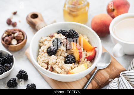 Bol de porridge d'avoine aux noisettes, de pêche et de blackberry servi avec une tasse de café. Un petit-déjeuner sain, la saine alimentation, régimes concept Banque D'Images