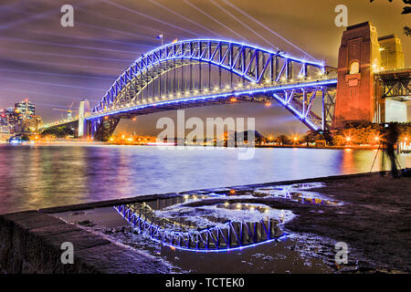 Passage en acier massif du Sydney Harbour Bridge sur le port de Sydney se reflétant dans flaque avec des faisceaux laser bleu ciel foncé à Vivid Sydney light show. Banque D'Images