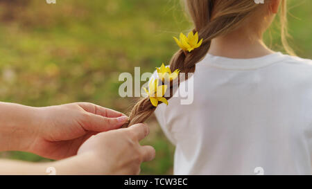 Prendre soin des mains maternelle braid les cheveux de petite fille. Maman décore ses cheveux en tressage jaune fleurs forêt vivent en fibre amorce. Professionnels de la maternité. Enfant ca Banque D'Images