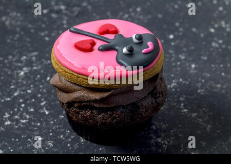 Valentines Day cupcake isolé sur fond marbré noir - fun cupcake avec guitare noir et deux cœurs avec glaçage rose décoré sur le chocolat Banque D'Images