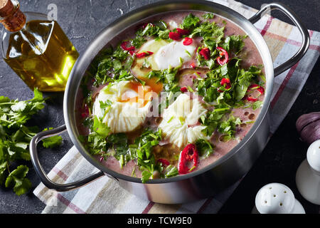 Des haricot soupe avec les oeufs pochés et de la coriandre dans une casserole de métal sur une table en béton avec une cuillère en bois et d'ingrédients, vue d'un Banque D'Images