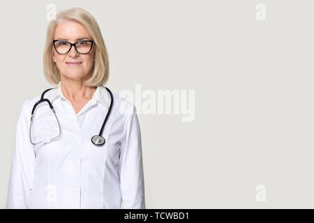 Attractive senior female doctor posing on grey background studio Banque D'Images