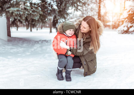 Jeune femme mère winter street, joue avec son jeune fils garçon 3 ans. Happy smiling, pesant jusqu'à rire, se réjouir. Veste chaude d'hiver. R Banque D'Images