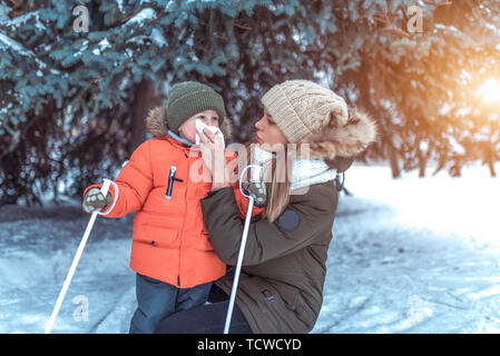 Une femme maman wipes son nez avec un mouchoir, télécharger serviette petit enfant, prendre soin de l'enfant au cours de la saison froide en hiver à l'extérieur, l'arrière-plan des bancs de neige de Banque D'Images