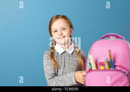 Closeup portrait de petite fille écolière avec sac à dos sur fond bleu. Retour à l'école. Le concept de l'éducation. Banque D'Images