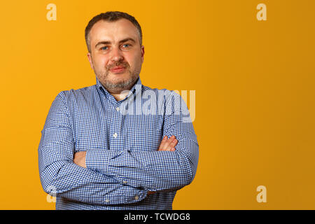 Homme sérieux, les bras croisés et une expression impassible posant devant un fond jaune. Copy space Banque D'Images