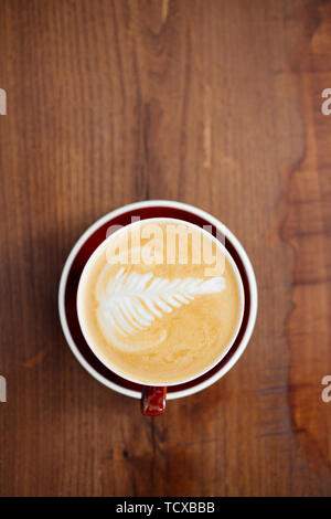 Une tasse de délicieux cappuccino dans une tasse rouge. Vue d'en haut au-dessus de la table en bois. Banque D'Images