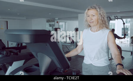 Senior woman est engagé sur un tapis roulant dans la salle de sport contre. Banque D'Images