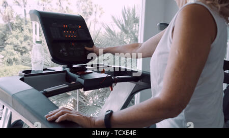 Senior woman est engagé sur un tapis roulant dans la salle de sport dans le contexte de la fenêtre panoramique. Banque D'Images