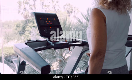 Senior woman est engagé sur un tapis roulant dans la salle de sport dans le contexte de la fenêtre panoramique. Banque D'Images