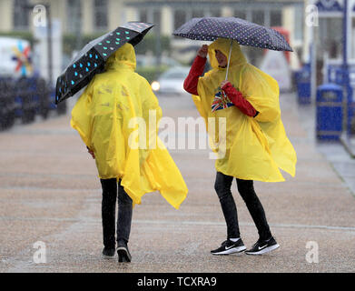 Deux étudiants d'échange allemand brave la pluie torrentielle sur la promenade, à Eastbourne, dans le Sussex, comme le prédit la pluie balaie le sud-est. Banque D'Images