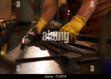 Close-up of méconnaissable workman en gants jaunes debout à table et mettre des outils sur elle tout en se préparant pour la soudure à l'arc Banque D'Images
