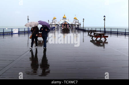 Les gens marchent le long de la jetée, à Eastbourne, dans le Sussex, comme le prédit la pluie balaie le sud-est. Banque D'Images