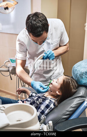 Portrait de la jolie petite fille d'ouvrir la bouche toute grande. Son médecin lui montre comment nettoyer les dents correctement. La médecine et les soins de concept. Sh verticale Banque D'Images