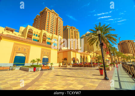 Des bancs et des palmiers le long de la promenade promenade marina à Porto Saoudite au Pearl-Qatar, Doha, avec en arrière plan les tours de bâtiments résidentiels Banque D'Images