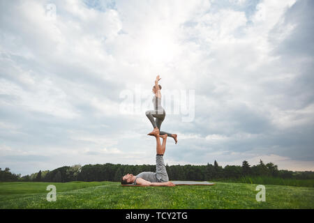 Des exercices d'équilibre. En bonne santé et jeune couple faisant yoga acrobatique dans la nature. Homme fort étendu sur une natte et équilibrage femme sur ses pieds. Lifesty sain Banque D'Images