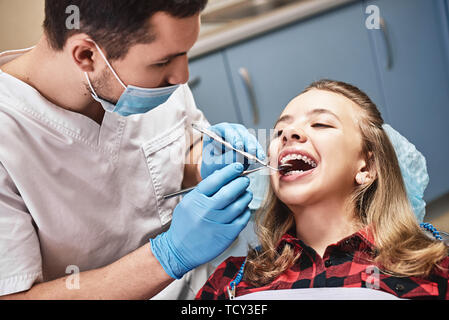 Fille blonde allongée dans fauteuil dentaire. Dentiste est contrôler ses dents à l'aide d'outils de dentiste. La médecine et les soins de concept. Close up Banque D'Images