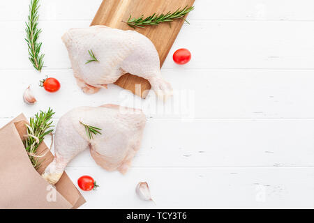 Creative haut voir télévision laïcs de matières premières fraîches des cuisses de poulet au romarin herbes ail tomates sur fond en bois blanc, avec l'exemplaire de l'espace. La préparation des aliments Banque D'Images