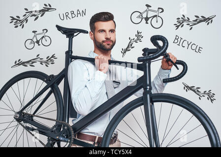 Best transport. La photo en gros du bon à l'homme dans les tenues de transporter son vélo en position debout contre l'arrière-plan gris avec la main doodl Banque D'Images