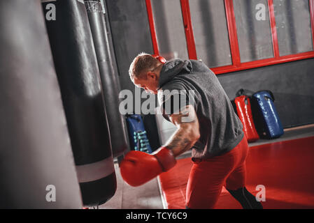 Confiant en rouge sportif musculaire gants de sport exercice sur sac lourd. Formation dur sur fond de sport boxe Banque D'Images