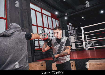 Disque de la formation. Confiant dans l'athlète tatoué musclé red gloves punching boxe avec pattes de couleur sur fond de sport partenaire Banque D'Images