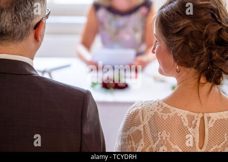 Décor de mariage : Couple assiste à la cérémonie de mariage avec la femme ceremnony master lire les journaux avec les anneaux de mariage sur la table. Banque D'Images