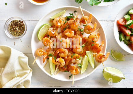 Brochettes de crevettes délicieux avec des greens, épices, citron vert et la sauce sur plaque blanche sur table en bois. Brochettes de crevettes grillées. De savoureux fruits de mer. Vue d'en haut, l' Banque D'Images