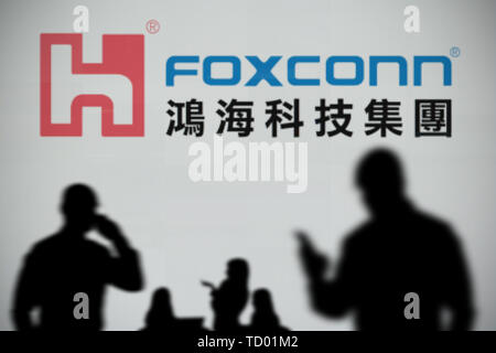 Le logo de Foxconn est vu sur un écran LED à l'arrière-plan tandis qu'une personne utilise la silhouette d'un smartphone dans l'avant-plan (usage éditorial uniquement) Banque D'Images