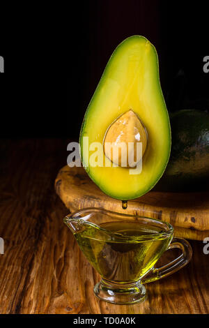Gouttes d'huile d'écouler dans un bol en verre. Fruit d'avocat et d'huile sur un plateau en bois sur la table. Banque D'Images