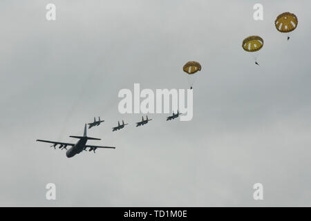 Les parachutistes de l'armée américaine sauter d'un C-130 de l'US Air Force comme l'US Air Force F-15's passent au-dessus au cours de la D-Day 75 opération aéroportée commémorative qui comprenait plus de 900 et 110 militaires parachutistes civils de sept pays de la fiere, France, le 9 juin 2019. Plus de 1 300 membres des services, en partenariat avec 950 hommes de toute l'Europe et le Canada, ont convergé dans le nord-ouest de la France pour commémorer le 75e anniversaire de l'opération Overlord, la Deuxième Guerre mondiale, alliés à l'invasion de Normandie, communément connu sous le nom de D-Day. (U.S. Photo de l'armée par le Cpl. Kevin Sterling Payne / libéré) Banque D'Images