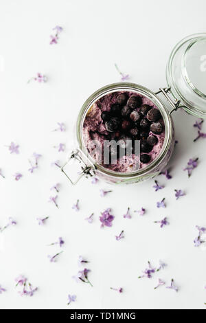 Petit déjeuner smoothie sain dans un bocal en verre avec fleurs lilas sur fond blanc Banque D'Images
