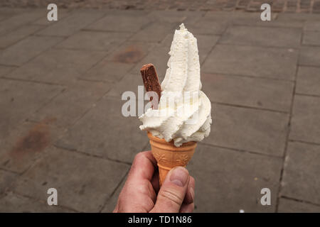 Gros plan d'un homme tenant la main avec une crème fouettée au chocolat glace flocon qui sort le côté, isolé contre un fond uni Banque D'Images