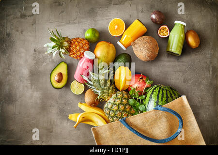 Grande variété de fruits tropicaux mûrs avec des jus déborde d'un plein sac shopping en tissu réutilisables sur ardoise texturé dans un concept de santé. Banque D'Images