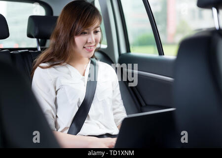 Belle asiatique young woman using laptop in car Banque D'Images