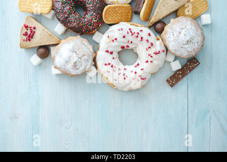 Les aliments sucrés nuisibles on blue background. Beignes, muffins, des chocolats sur la table pile. La notion de mauvaise alimentation et de l'embonpoint. Le point de vue f Banque D'Images