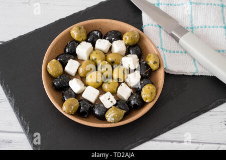 Une préparation d'olives vertes et noires servi dans un bol avec des petits carrés de fromage féta avec quelques herbes et l'huile. Banque D'Images