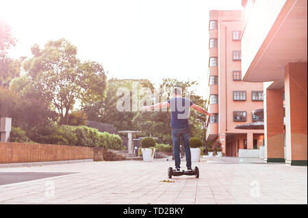 Un homme en jeans et baskets sur un hoverboard ride dans la ville. Happy boy riding autour au coucher du soleil. L'électronique moderne pour la détente et le divertissement Banque D'Images