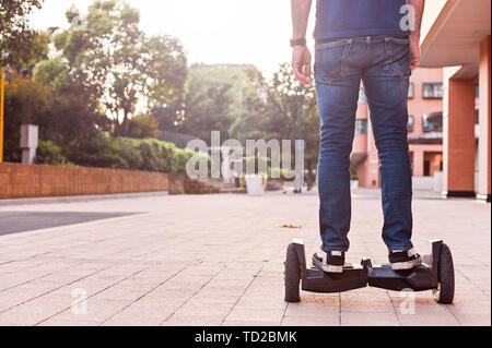 Un homme en jeans et baskets sur un hoverboard ride dans la ville. Happy boy riding autour au coucher du soleil. L'électronique moderne pour la détente et le divertissement Banque D'Images