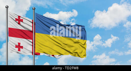 De brandir le drapeau de la Géorgie et de l'Ukraine dans le vent contre ciel bleu nuageux blanc ensemble. Concept de diplomatie, de relations internationales. Banque D'Images