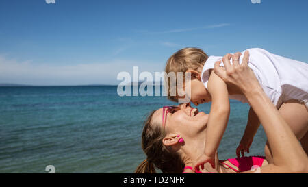 Heureux jeune mère jouant avec son enfant fille dans son levage couches par la mer au printemps. Banque D'Images