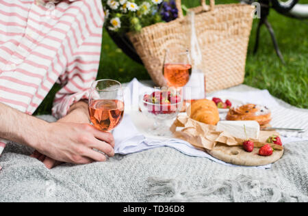 Man's hand holding verre de vin rose d'été, pique-nique avec vin et fromage sur la pelouse dans le parc de la ville close-up Banque D'Images