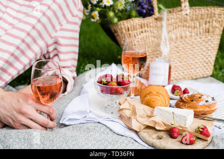 Man's hand holding verre de vin rose d'été, pique-nique avec vin et fromage sur la pelouse dans le parc de la ville close-up Banque D'Images