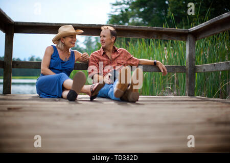 Mature Woman sourire et chat, assis ensemble sur une jetée en bois sur un lac. Banque D'Images