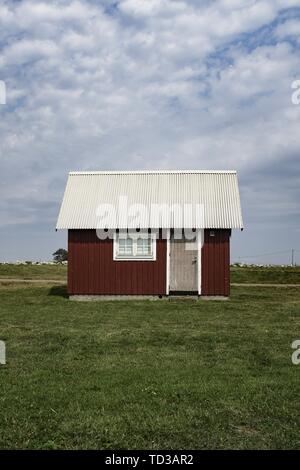 Grange rouge en bois avec un toit blanc dans un grand champ vert avec ciel bleu nuageux Banque D'Images