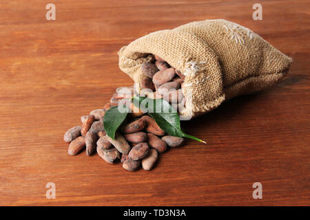 Les fèves de cacao dans le sac avec des feuilles sur fond de bois Banque D'Images