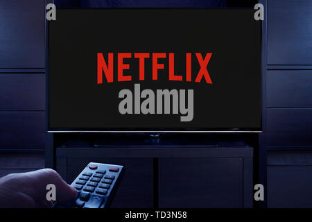 Un homme d'un points TV remote à la télévision qui affiche le logo de la vidéo à la demande Netflix streaming service (usage éditorial uniquement). Banque D'Images
