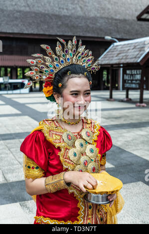 Makassar, Sulawesi, Indonésie - 28 Février 2019 : jeune femme en costume traditionnel local. Rouge et jaune contre le palais en bois brun foncé Banque D'Images